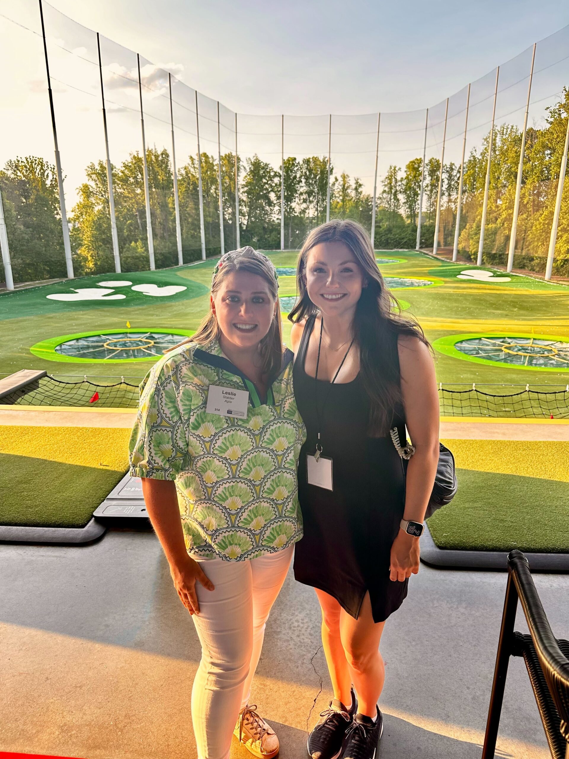 Two Women at Top Golf standing Infront of the putting area smiling at the camera.
